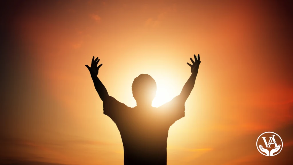 Silhueta de um homem com braços erguidos em adoração contra um pôr do sol vibrante em tons de laranja e dourado. No canto inferior direito, o logotipo branco 'VA' do blog Vida que Abençoa. A imagem transmite espiritualidade, gratidão e liberdade cristã.